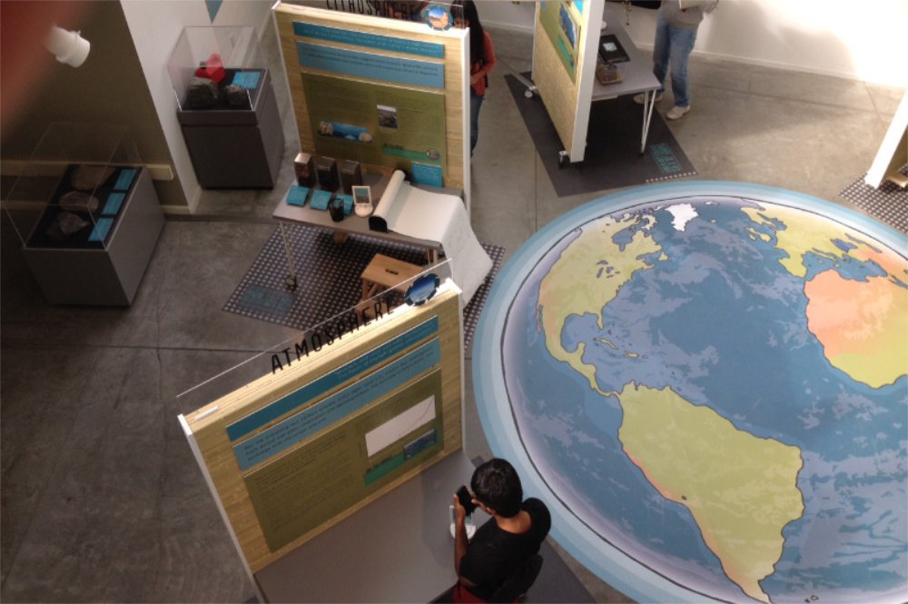 Image from above of a museum exhibit with a large picture of the Earth on the floor.