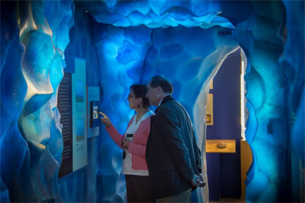 Photo of two people inside part of a museum exhibit that looks like a blue ice tunnel.